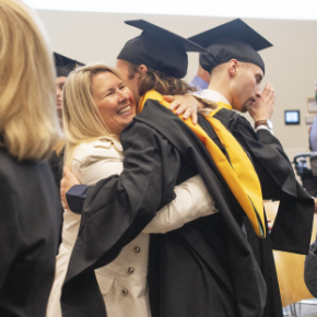 Students in cap and gown embraces a family member.